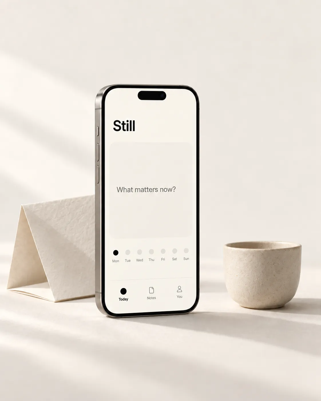 A phone showing the Still journaling app beside a ceramic cup
